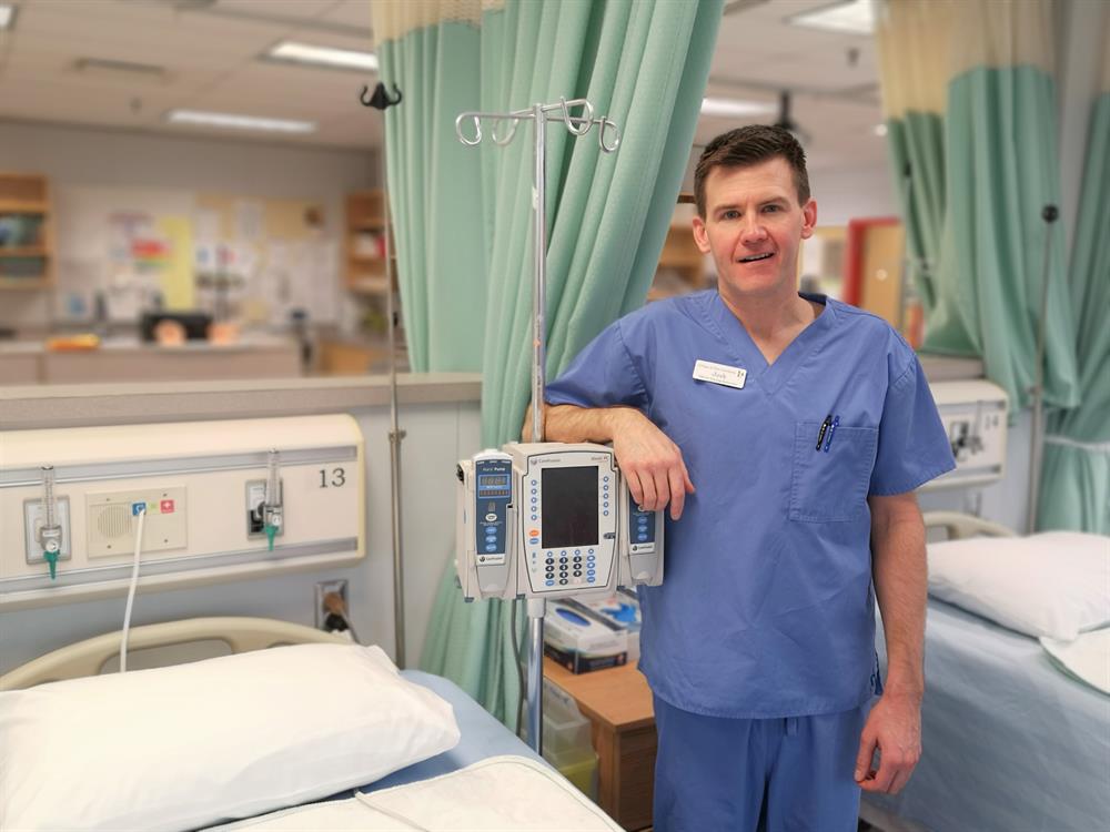 Josh Staub a Licensed Practical Nurse standing next to monitoring equipment