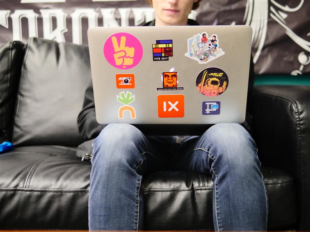 Student working on a Macbook sitting on a leather couch