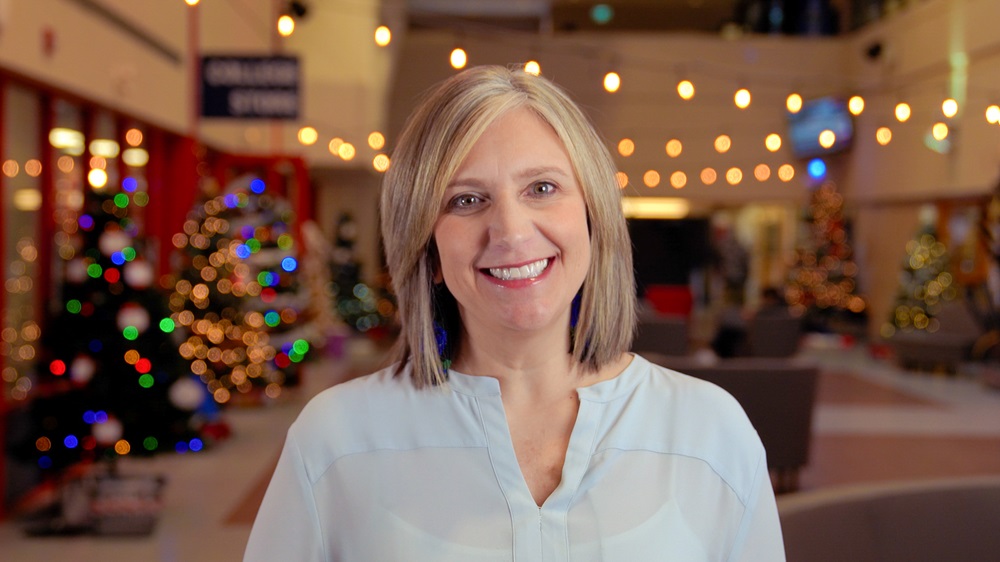 CNC President, Cindy Heitman, smiling at the camera with soft Christmas lights behind her