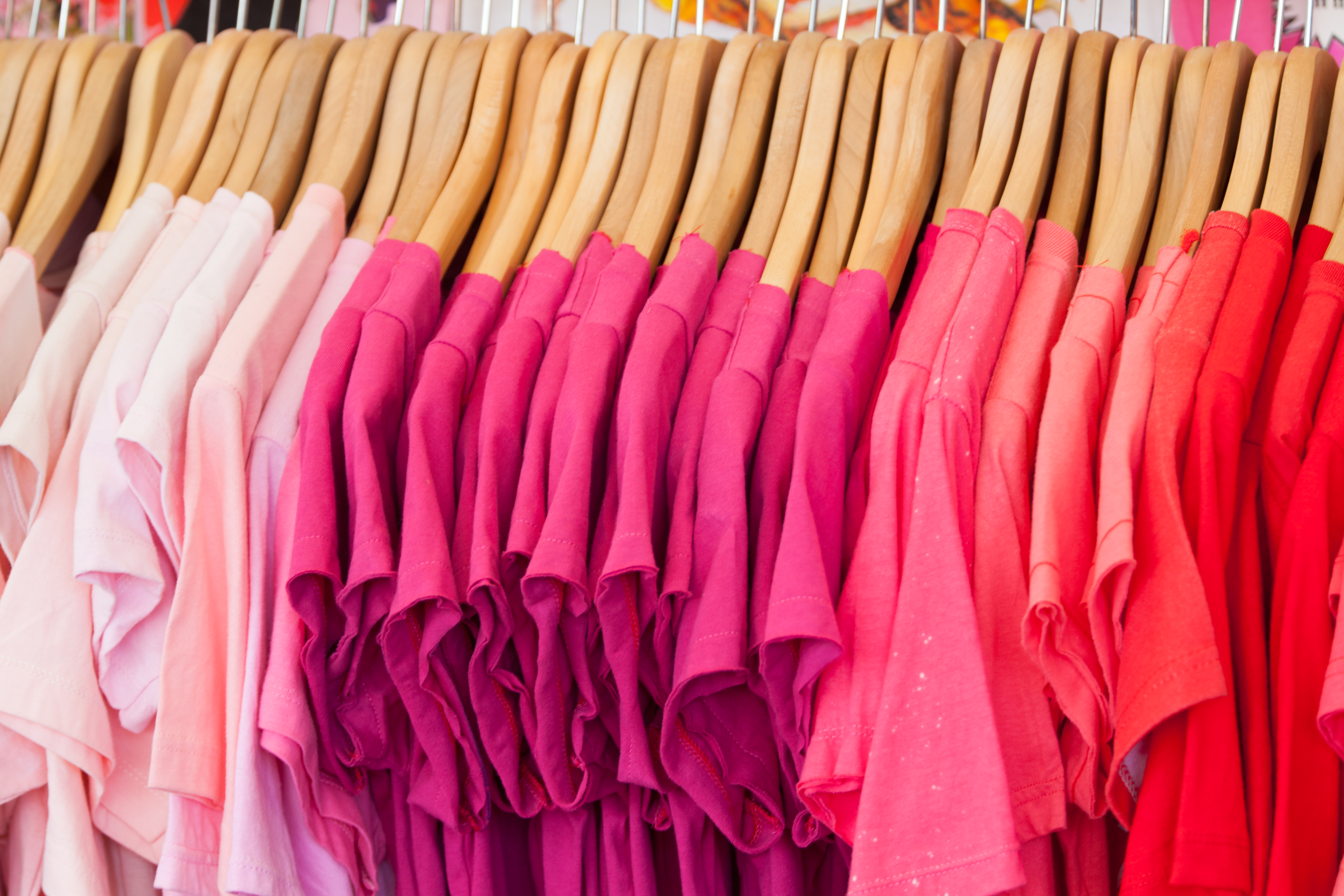 Many shades of pink shirts hanging on rack