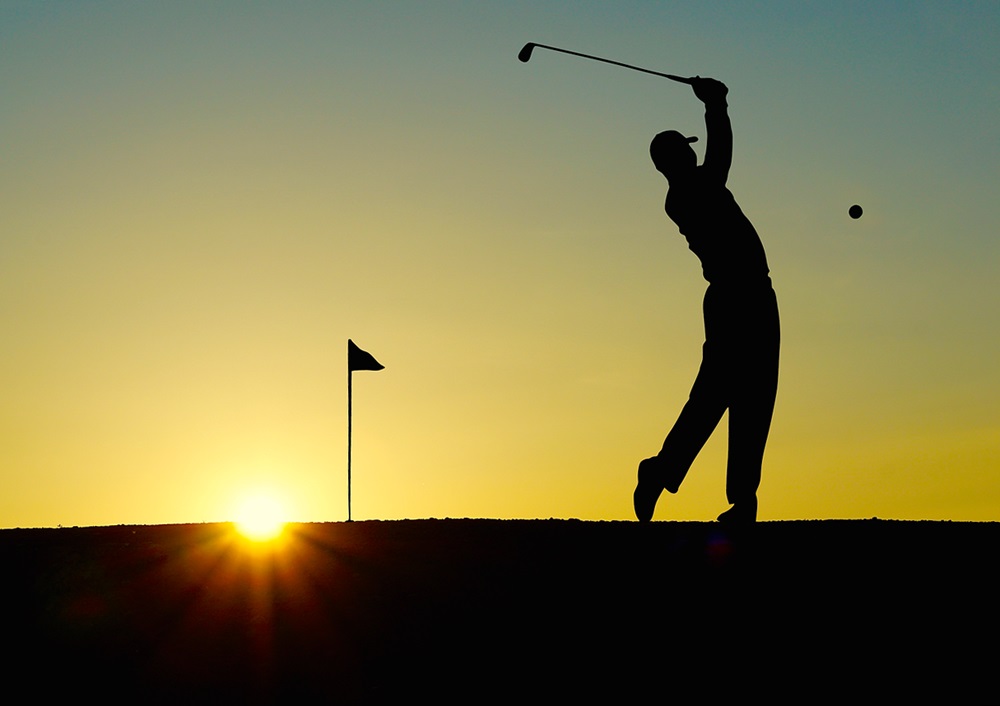 Silhouette of a golfer chipping the ball into the sunset