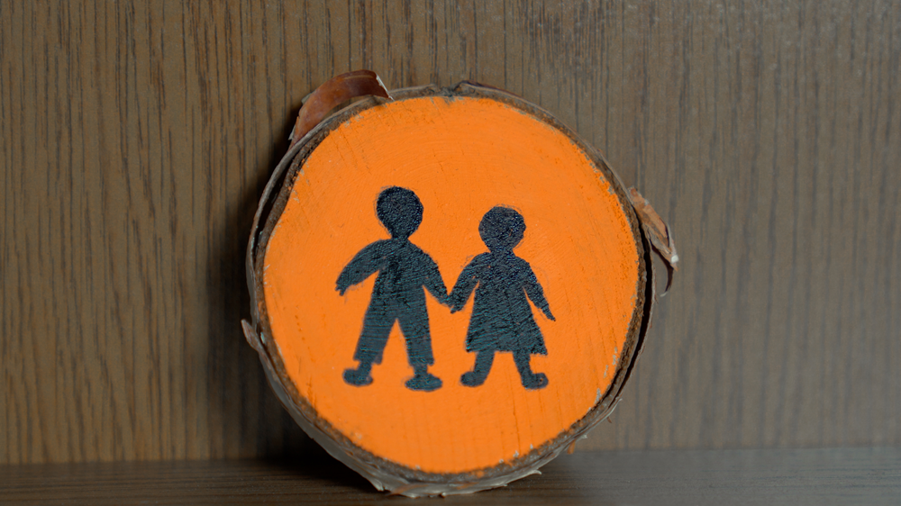 cross-section of a tree painted orange, with two black silhouettes of a boy and a girl