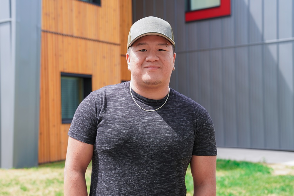 Darian stands in front of Nahoonai-a student housing wearing a cap