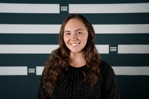 Kyndra standing in front of CNC backdrop, smiling